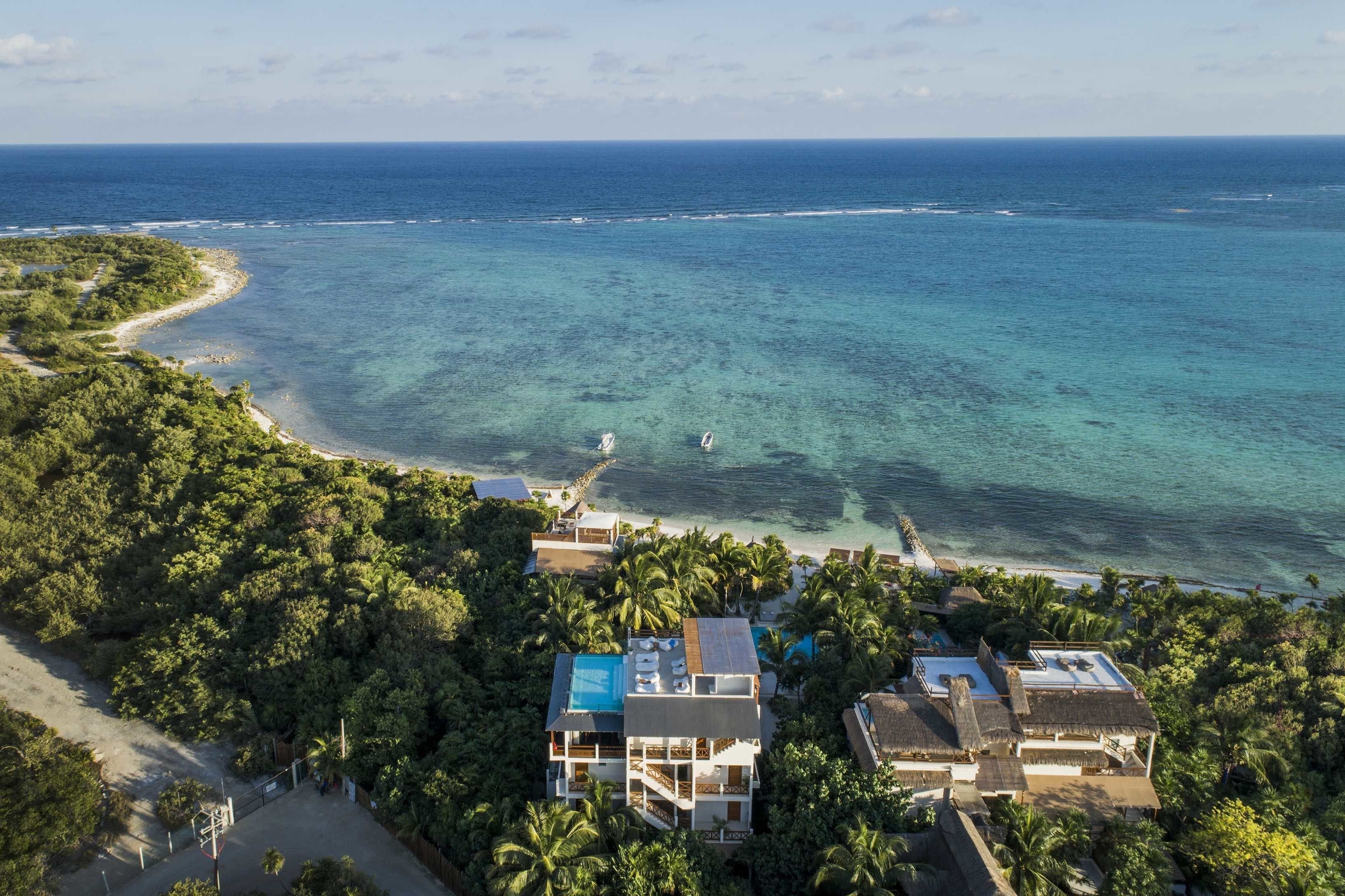 An aerial view of a coastal resort with multiple buildings, a beach, and a clear view of the ocean.