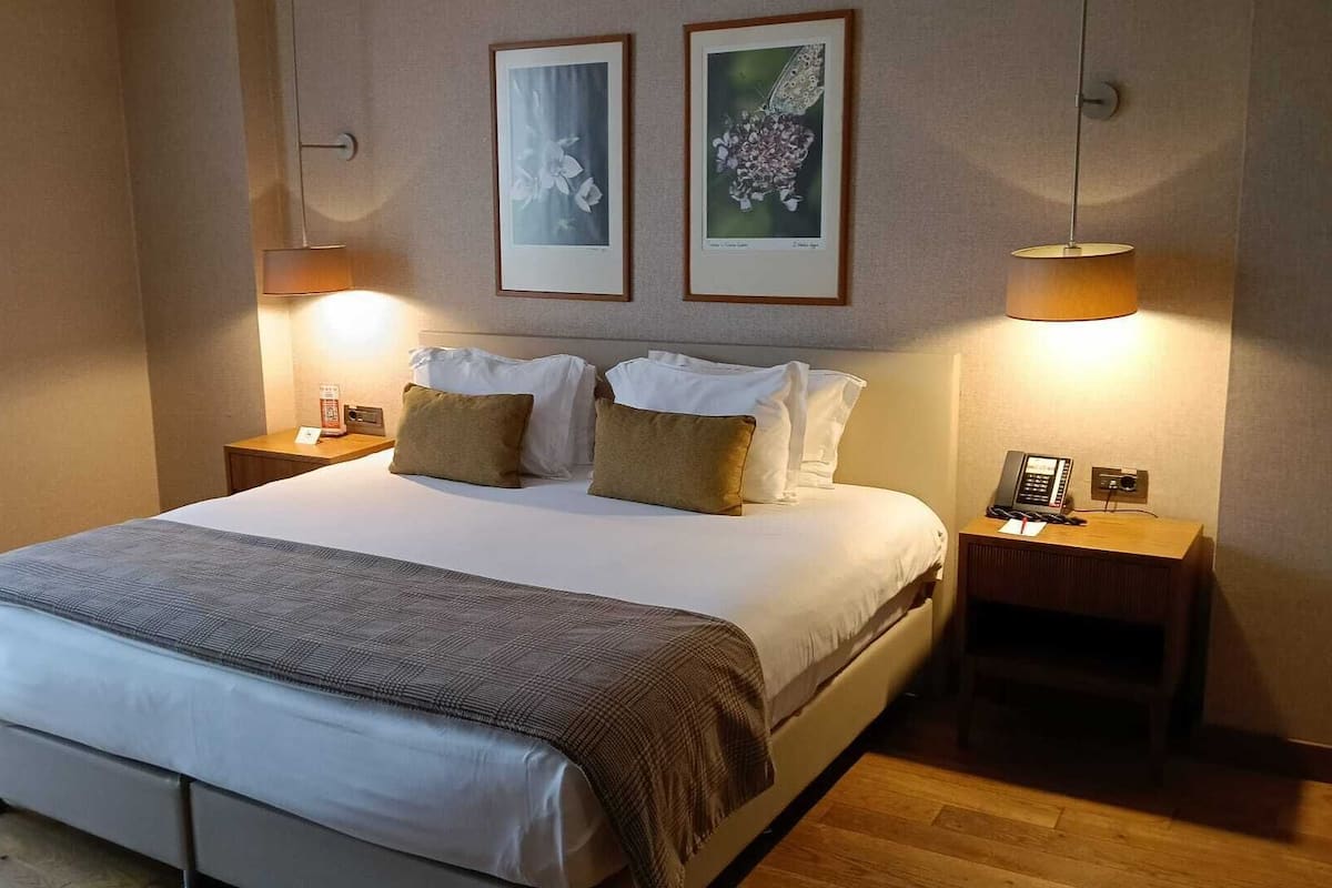 Een hotelkamer met een groot bed, twee nachtkastjes, een lamp en twee ingelijste foto's aan de muur.
