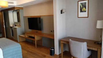 Habitación de hotel con cama, escritorio, televisión, espejo y un cuadro en la pared.