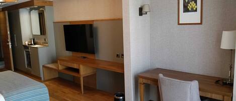 A hotel room with a bed, a desk, a television, a mirror, and a framed picture on the wall.