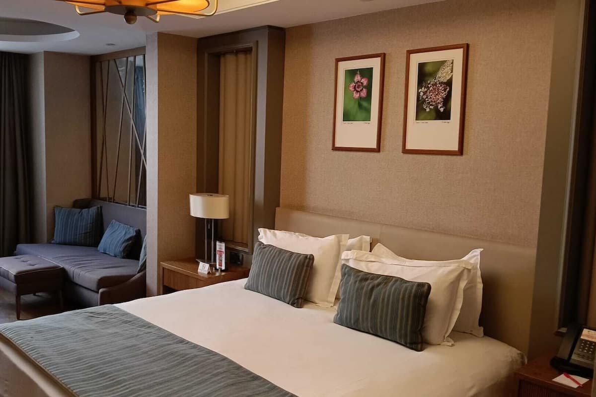 Een hotelkamer met een groot bed, een bank, een bureau met een lamp en twee ingelijste foto’s aan de muur.