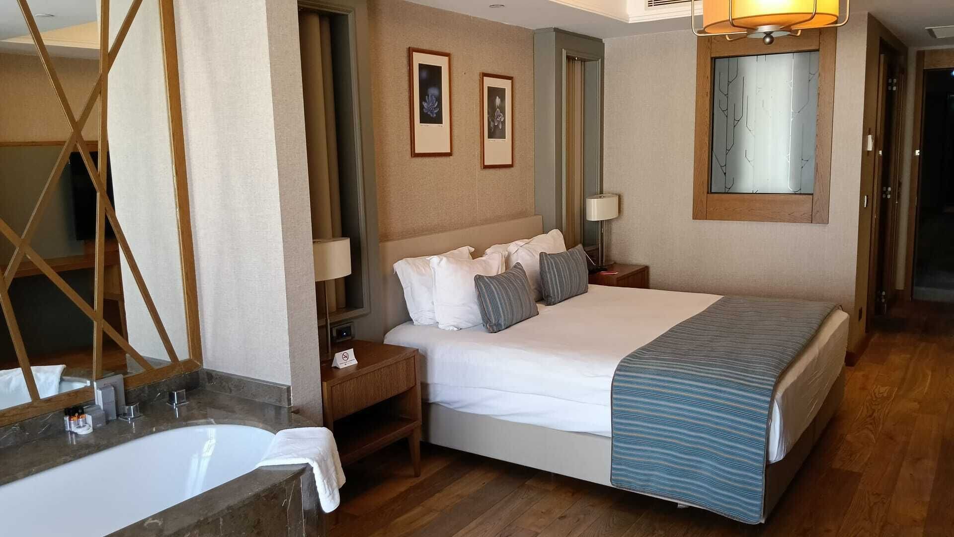Ein Hotelzimmer mit einem großen Bett, einem Badezimmer mit Badewanne, einem Holzboden und gerahmten Bildern an der Wand.