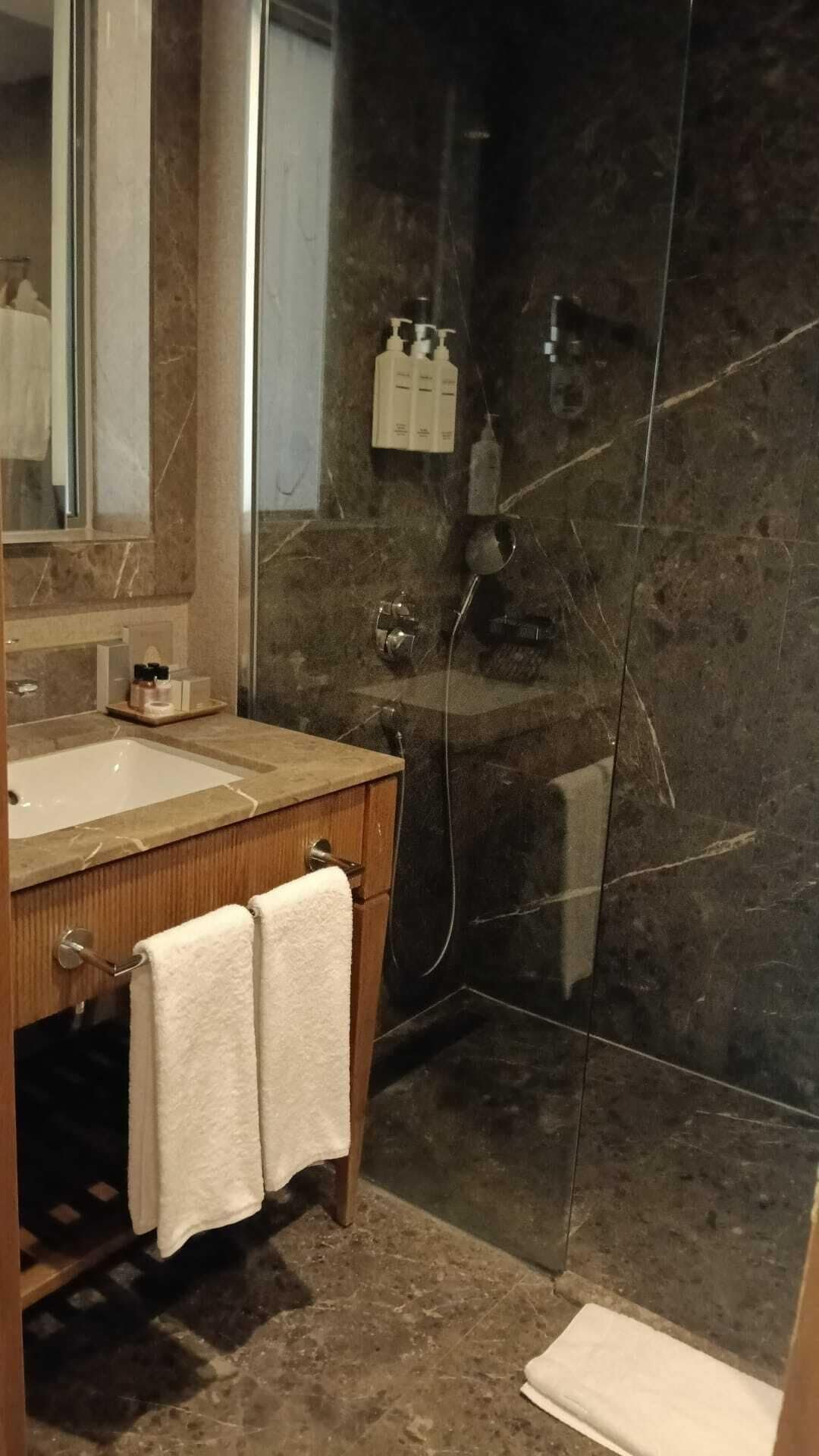 A bathroom with a marble sink, a mirror, a towel rack, and a shower area.