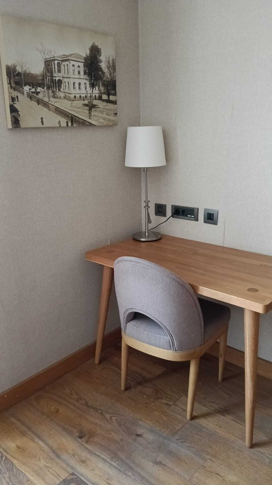 A room with a wooden desk, a chair, a lamp, and a wall-mounted picture.