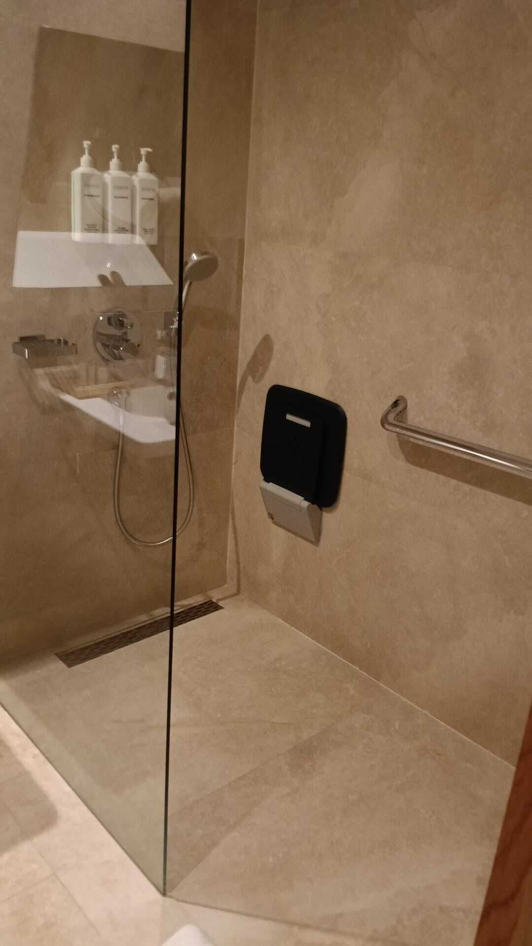 A bathroom with a glass shower enclosure, a sink, and a soap dispenser mounted on the wall.