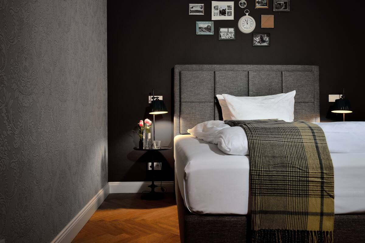 A hotel room with a large bed, a bedside table with a lamp, and a wall with framed pictures.