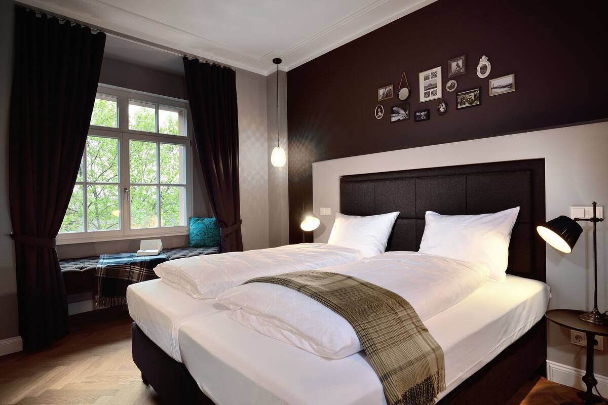 A well-lit bedroom with a large bed, a desk, and a window with curtains.