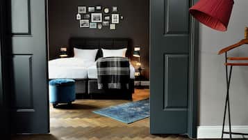 Un dormitorio con cama, mesitas de noche, un otoman azul, una lámpara roja y una pared adornada con cuadros.