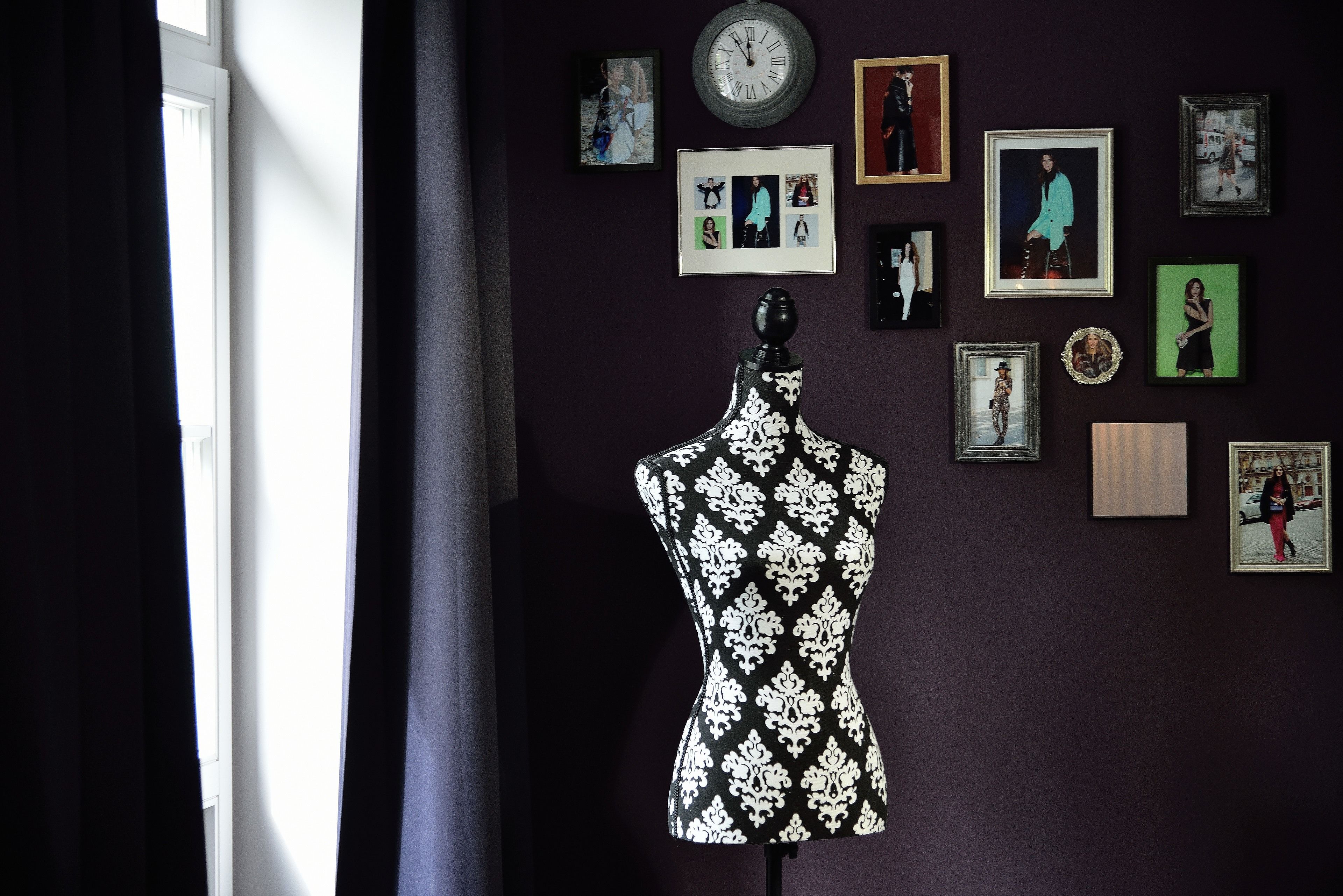 A mannequin in a room with a dark wall, a clock, and various framed pictures.