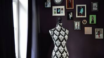 A mannequin in a room with a dark wall, a clock, and various framed pictures.