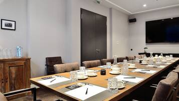 Un salón de conferencias con una larga mesa, sillas de cuero marrón y una amplia pantalla de televisión en la pared.