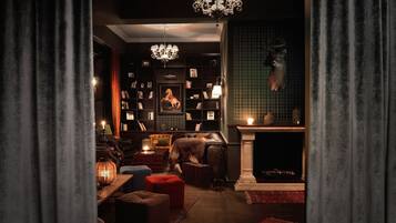 Una biblioteca acogedora y con poca luz, con chimenea, sillones de cuero y un candelabro.