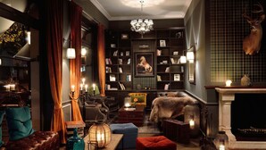 Una sala de estar acogedora y bien iluminada, con chimenea, una cabeza de ciervo decorativa y una estantería llena de libros.
