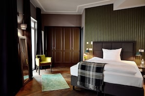 A hotel room with a large bed, a chair, a wardrobe, and a green wall.