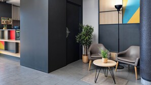 Een moderne lobby met een donkere muur, een houten receptiebalie, een potplant, twee leren fauteuils en een vloerlamp.