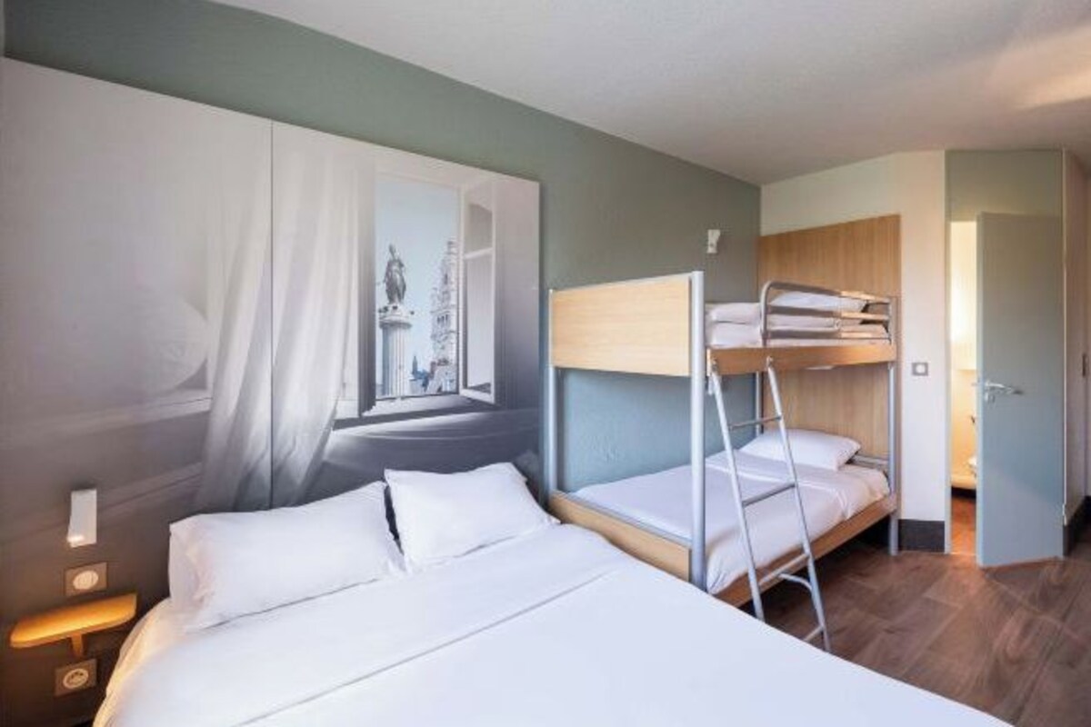 Habitación de hotel con literas, una cama individual, una mesita de noche y un cuadro en la pared.