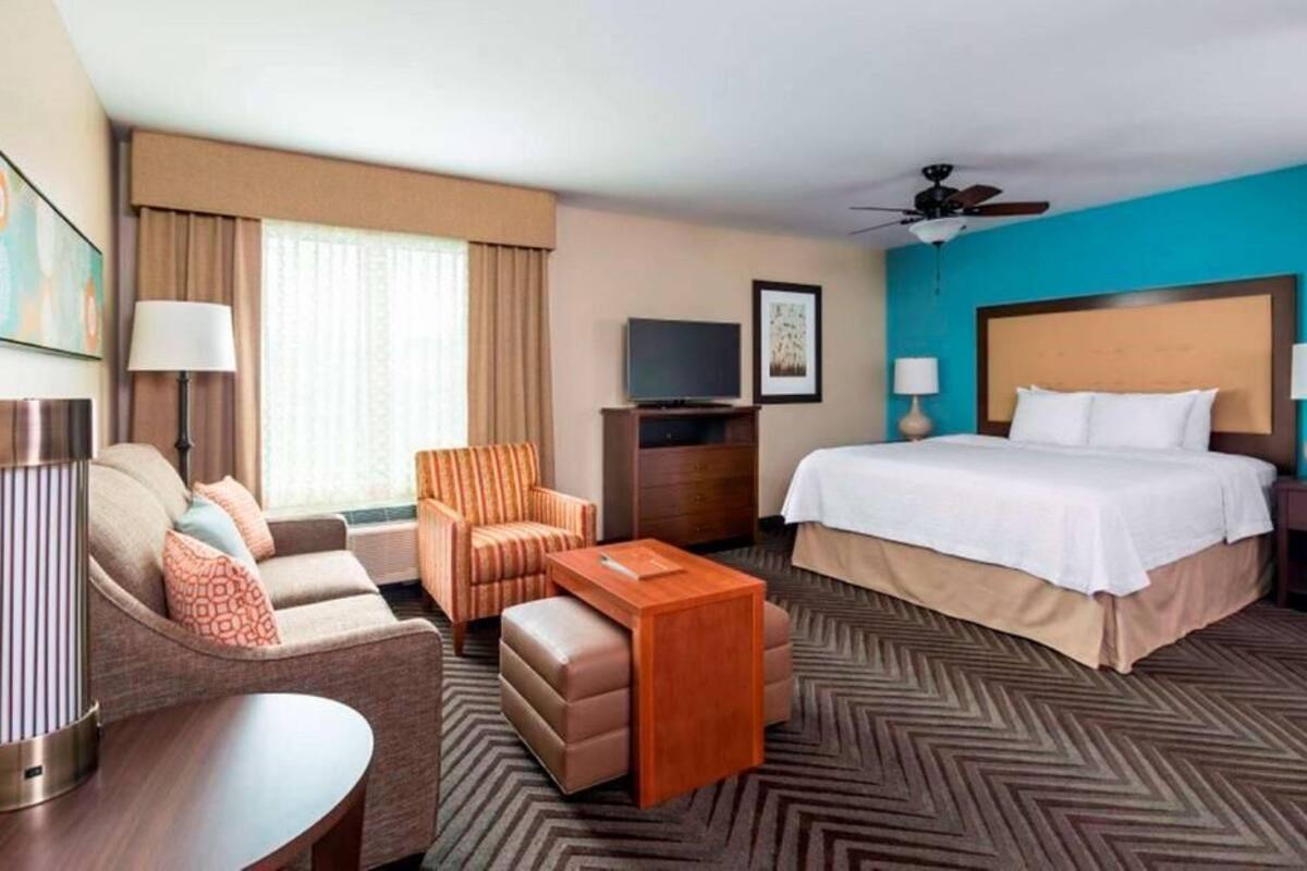 A hotel room with a bed, a sofa, a coffee table, a TV, and a ceiling fan.
