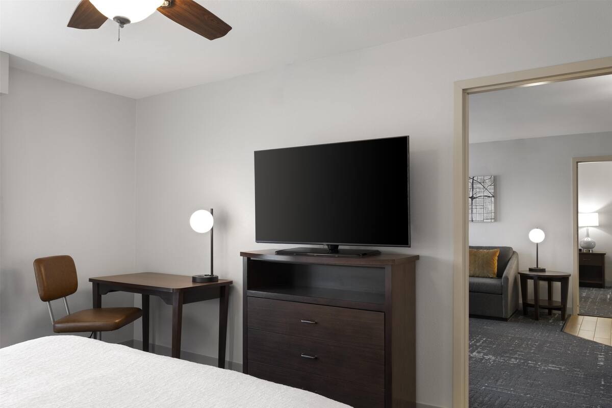 Ein Hotelzimmer mit Bett, Schreibtisch, Stuhl, Fernseher und Spiegel.