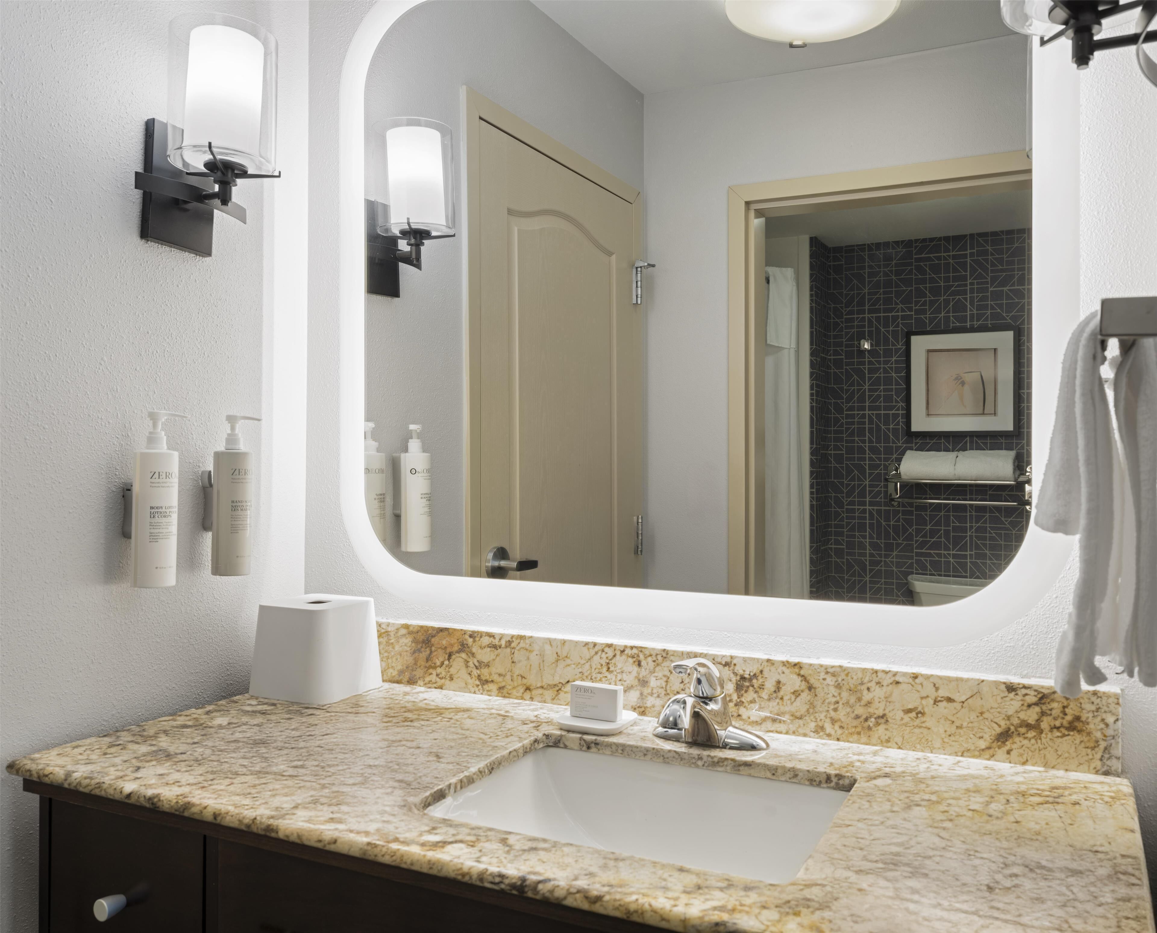 Une salle de bain avec un lavabo en marbre, un grand miroir et des articles de toilette fixés au mur.