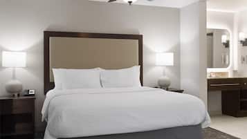 A hotel room with a large bed, two bedside tables with lamps, a ceiling fan, and a bathroom with a vanity and mirror.