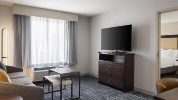Habitación de hotel con cama, televisión en una cómoda, escritorio con silla y ventana con cortinas.