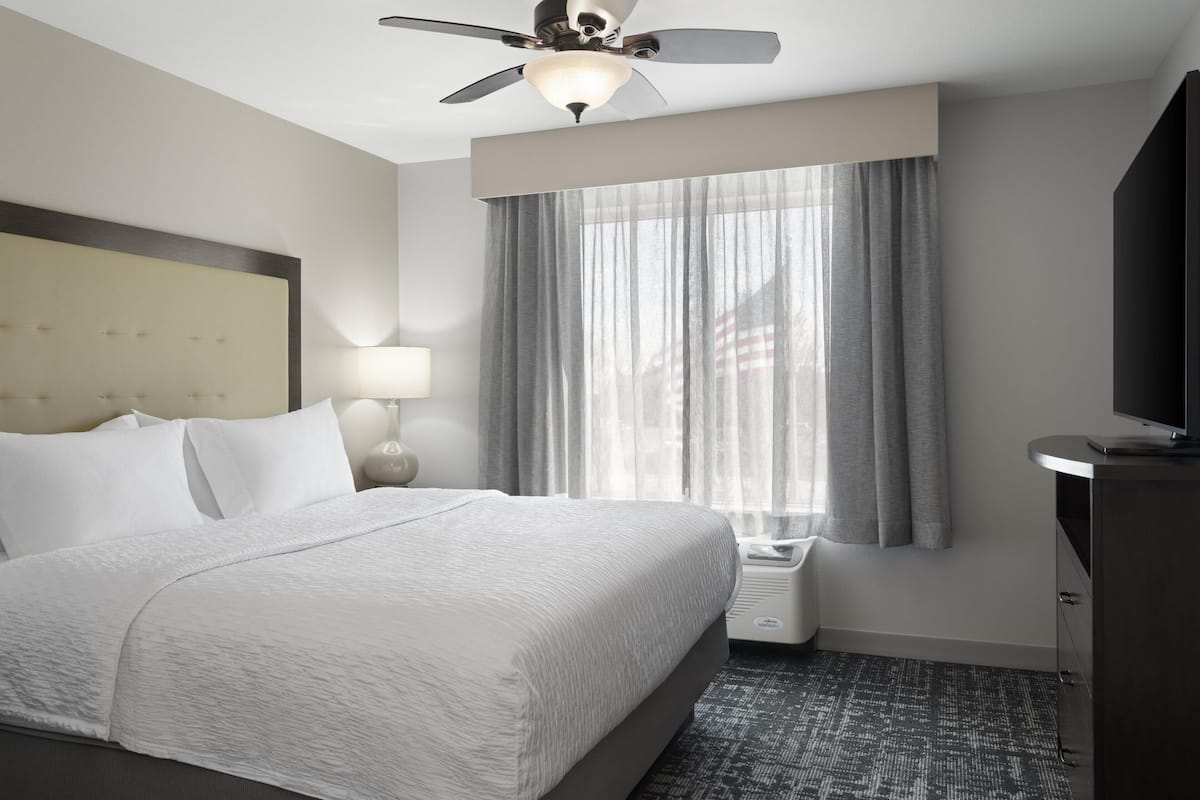 Ein Hotelzimmer mit Bett, Deckenventilator, Fernseher und einem Fenster mit Vorhängen.