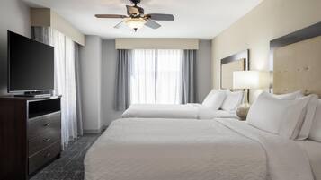 A hotel room with two beds, a TV, a ceiling fan, and a window with curtains.