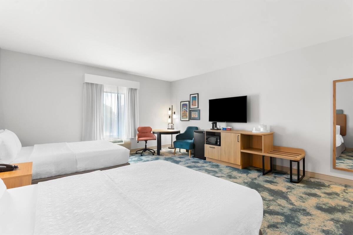 A hotel room with a large bed, a desk with a computer, a TV, and a seating area with chairs.