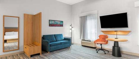 Hotellihuone, jossa on sininen sohva, puinen vaatekaappi, litteänäyttöinen televisio, pyöreä pöytä ja tuoli.