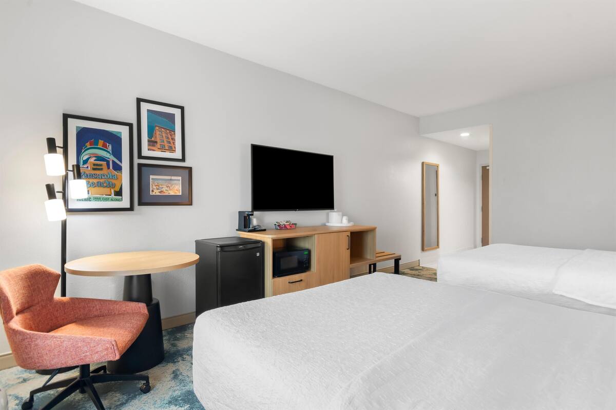 A hotel room with a bed, a desk with a computer, a chair, a TV, and a microwave.