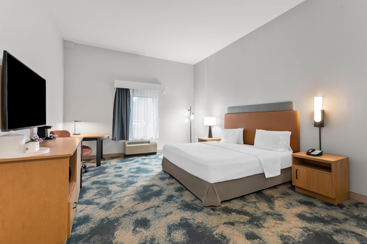 A hotel room with a bed, bedside tables, a desk, a flat-screen TV, and a window with curtains.