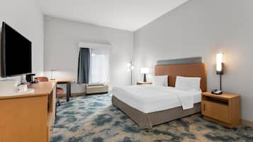 Ein Hotelzimmer mit Bett, Nachttischen, Schreibtisch, Flachbildfernseher und einem Fenster mit Vorhängen.