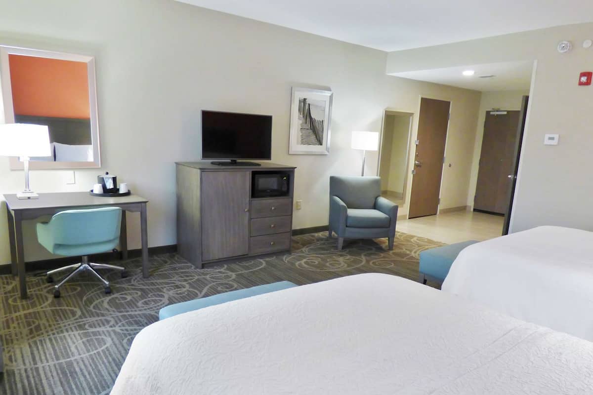 A hotel room with a bed, a desk with a computer, a television, a chair, and a door.