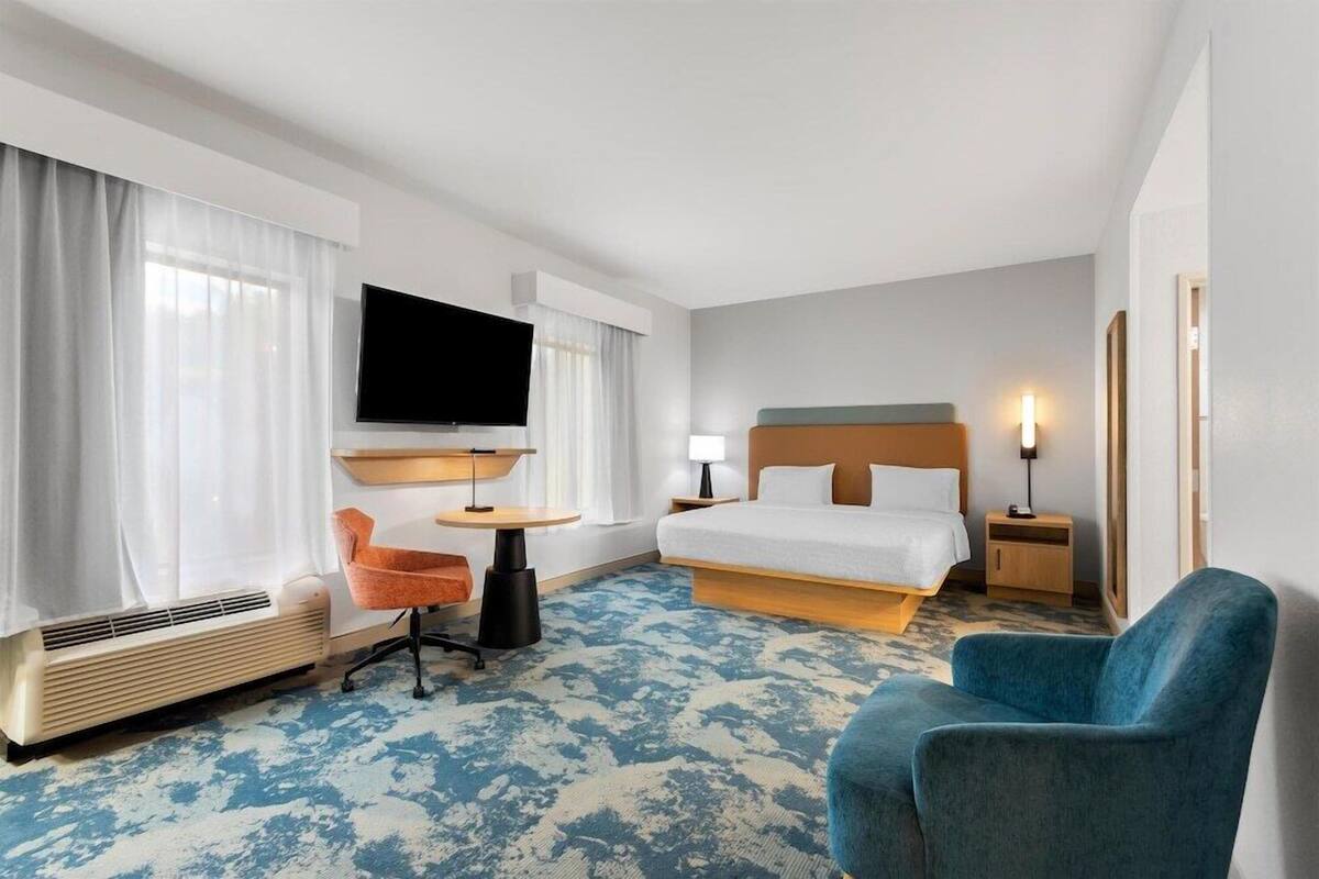 A hotel room with a bed, a TV, a desk, a chair, and a heater.