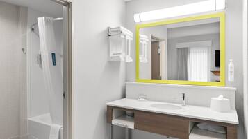 Une salle de bain moderne avec une douche, un lavabo, un miroir avec un cadre jaune et des serviettes soigneusement rangées.