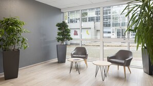 A modern indoor space with two grey armchairs, a small round table, and large potted plants. - B&B HOTEL Lyon Centre Monplaisir (Lyon)