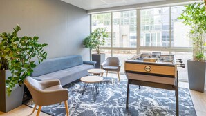 A room with a sofa, two chairs, a foosball table, and a large window with a city view. - B&B HOTEL Lyon Centre Monplaisir (Lyon)