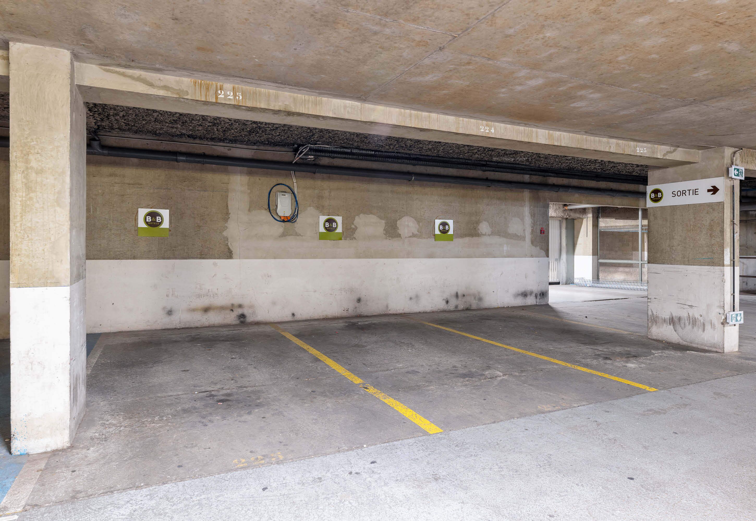 Garagem subterrânea com paredes de concreto, linhas de estacionamento amarelas e uma placa indicando a saída.
