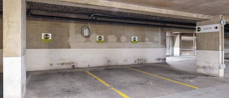 Garagem subterrânea com paredes de concreto, linhas de estacionamento amarelas e uma placa indicando a saída.