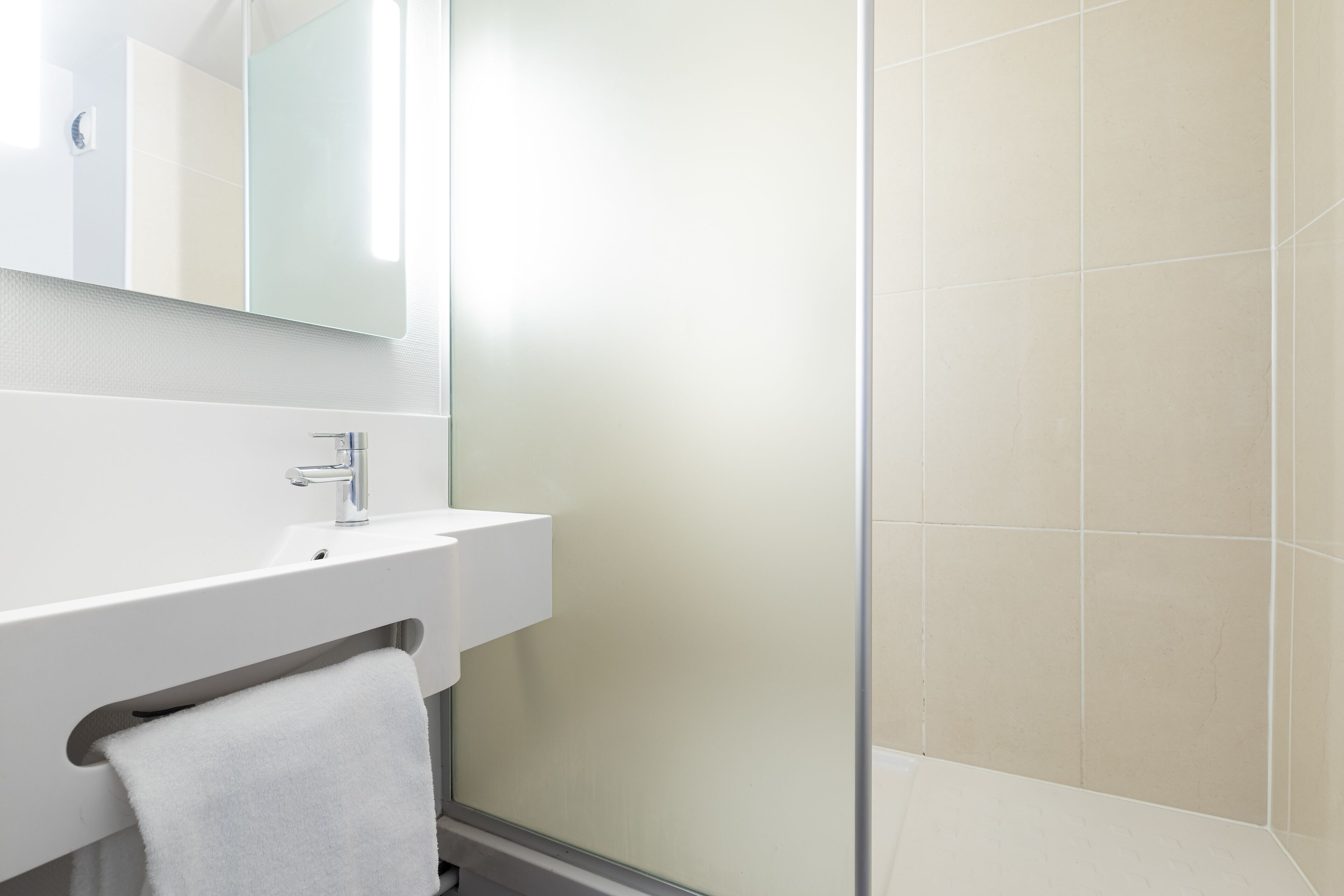 A modern bathroom with a white sink, mirror, and glass shower enclosure.