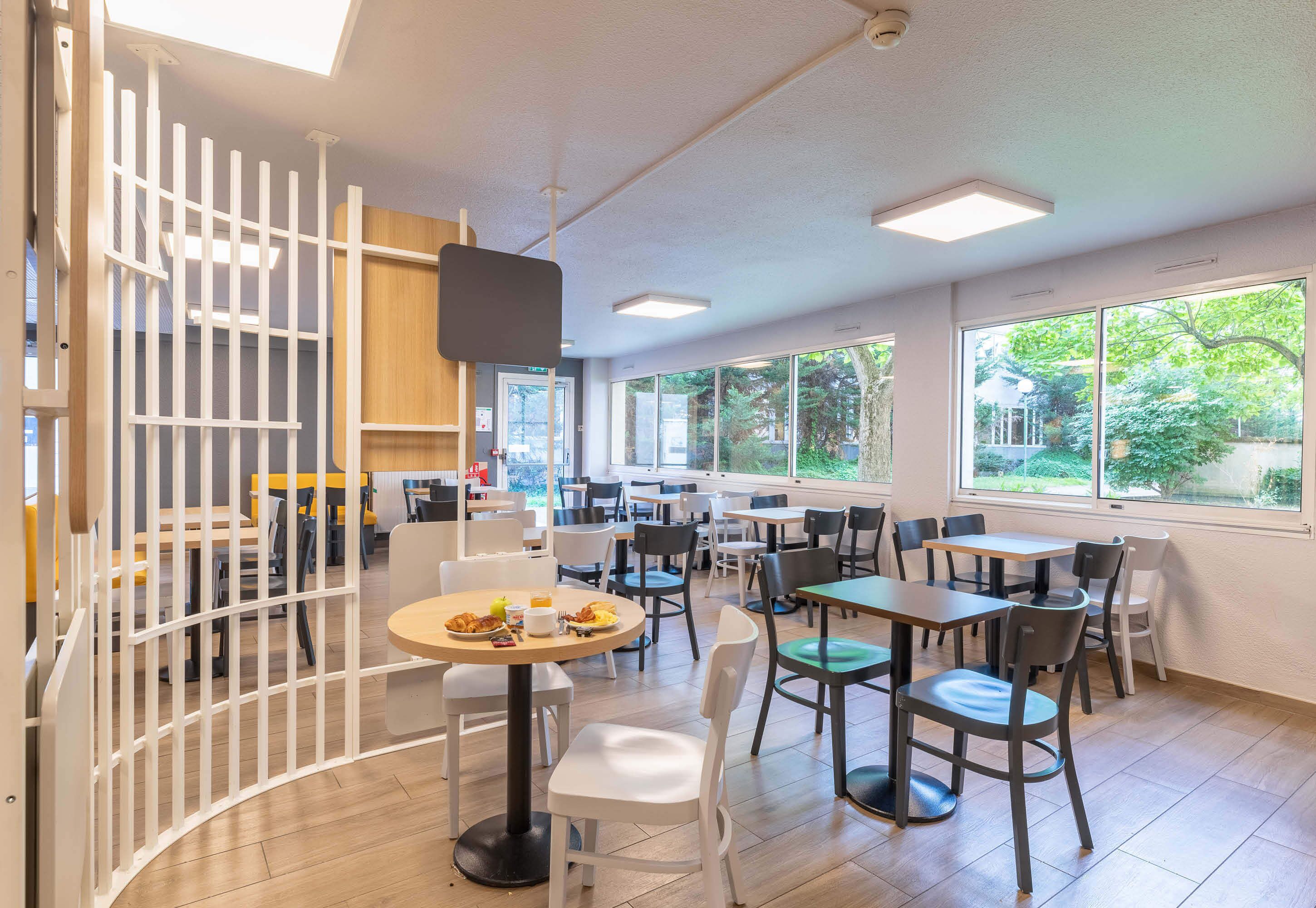 A modern dining area with round tables and chairs, large windows, and a white partition.