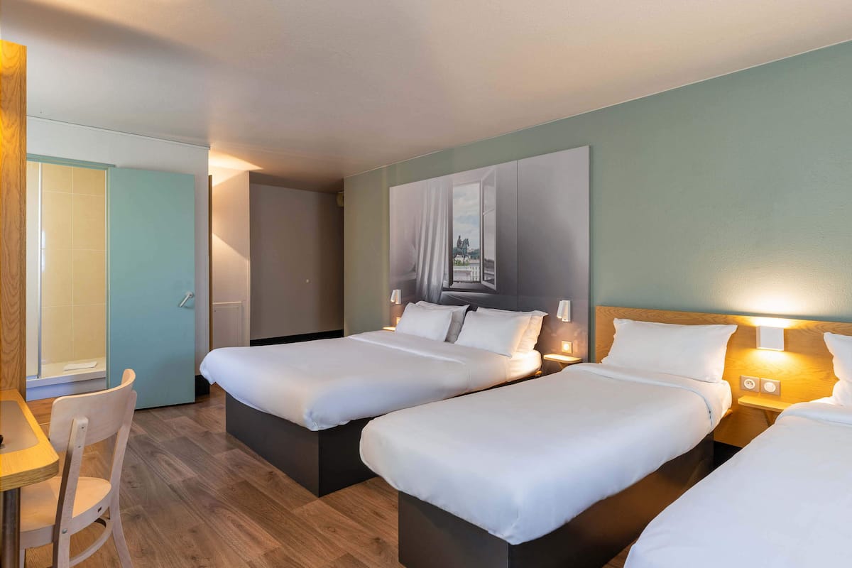 Quarto de hotel com duas camas, uma escrivaninha e uma cadeira.