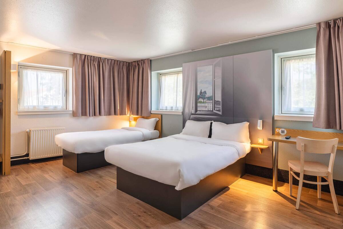 Quarto de hotel com duas camas, uma escrivaninha e uma cadeira.