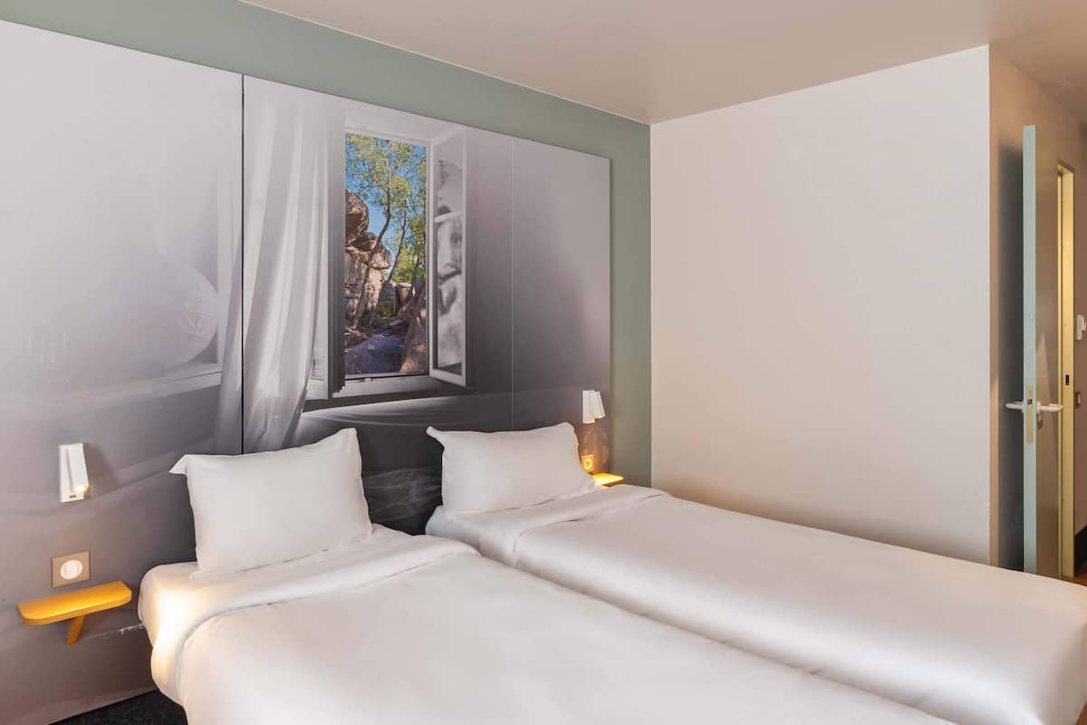 Quarto de hotel com uma cama, uma janela com vista para árvores e uma porta.