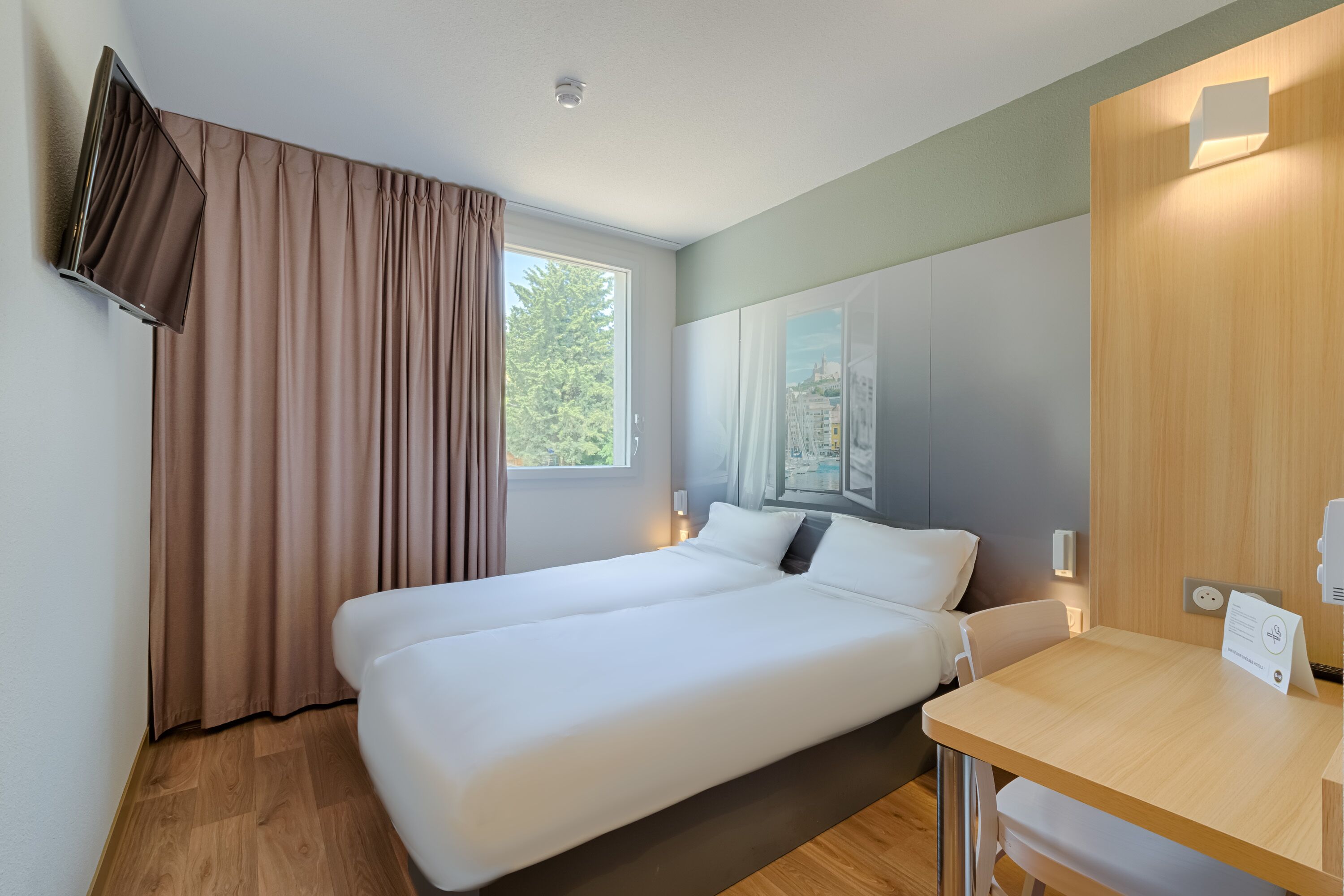 A hotel room with a bed, a desk, and a window with curtains.
