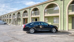 A row of motel rooms with arched windows and balconies, a black car parked in front, and a stairway leading to the entrance. - Sienna Inn Channelview, TX (Channelview)