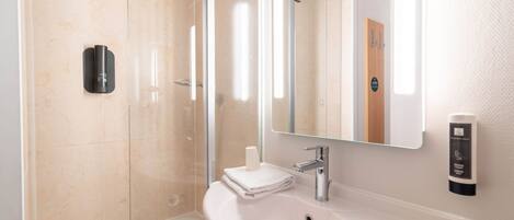 Un baño moderno con cabina de ducha de vidrio, un lavamanos blanco con espejo y dispensador de gel antibacterial.