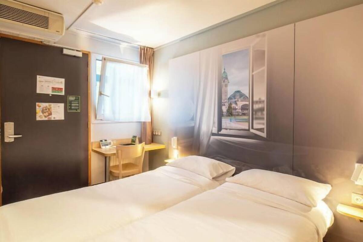 A hotel room with a bed, a desk, a chair, and a wall with a window view.