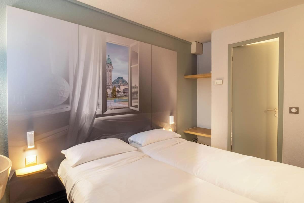 A hotel room with a bed, a nightstand, a wall-mounted shelf, and a door.