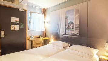 A hotel room with two beds, a desk, a chair, a window with curtains, and a wall-mounted air conditioner.
